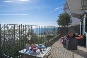 A balcony with a table set for dining, overlooking a coastal view. - Casa Cetrangolo - Panoramic House a few Steps From the sea (Praiano)