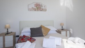 A neatly made bed with white and patterned pillows, a bedside table with a lamp, and a wall-mounted artwork.