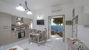A modern kitchen with a dining area, a TV mounted on the wall, and a view of the sea through an open door.