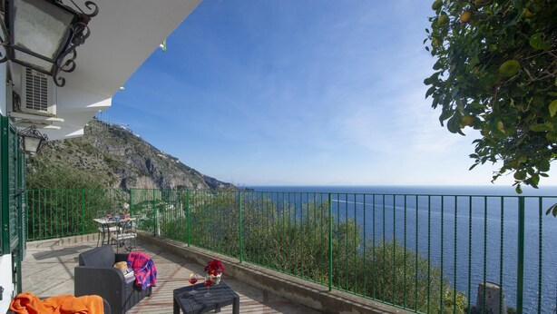 A terrace with outdoor seating, a view of the sea, and a mountainous backdrop.