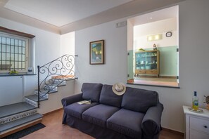 A living room with a sofa, a framed picture on the wall, a staircase with a metal railing, and a kitchen area visible through a window. - Casa Cimino A - Lovely Apartment and Amazing View on Capri and Positano (Praiano)