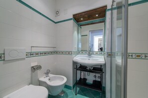 A bathroom with white tiles, a sink, a bidet, and a shower. - Casa Cimino A - Lovely Apartment and Amazing View on Capri and Positano (Praiano)