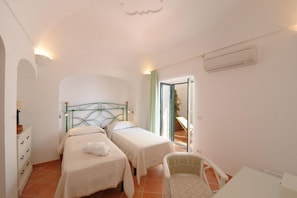 A bedroom with two beds, a chair, a desk, and an air conditioning unit. - Casa Alessia - Big Terrace on the sea Ideal for Large Families (Praiano)