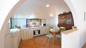 Une cuisine avec des meubles blancs, un pare-feu en carrelage, une cuisinière et un coin repas comprenant une table et des chaises.