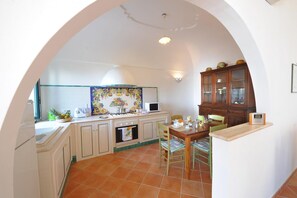 A kitchen with white cabinets, a tiled backsplash, a stove, and a dining area with a table and chairs. - Casa Alessia - Big Terrace on the sea Ideal for Large Families (Praiano)