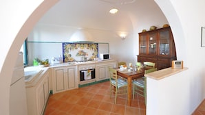 A kitchen with white cabinets, a tiled backsplash, and a dining area with a wooden table and chairs. - Casa Giorgia - Exclusive Panoramic Villa in the Heart of Praiano (Praiano)