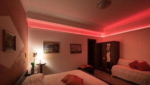A hotel room with a bed, a bedside table with a lamp, a small table with a plant, and a painting on the wall. - Villa Gioiello - Sea View Pool With Chromotherapy (Amalfi)