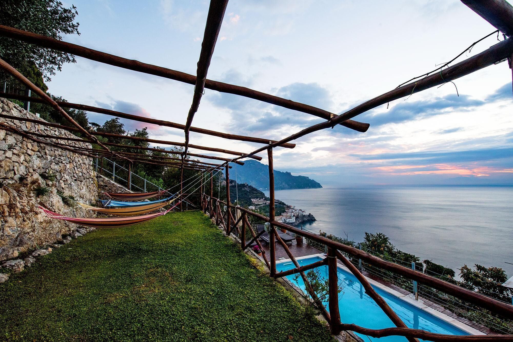 A hammock on a stone wall overlooking a pool and the sea.
