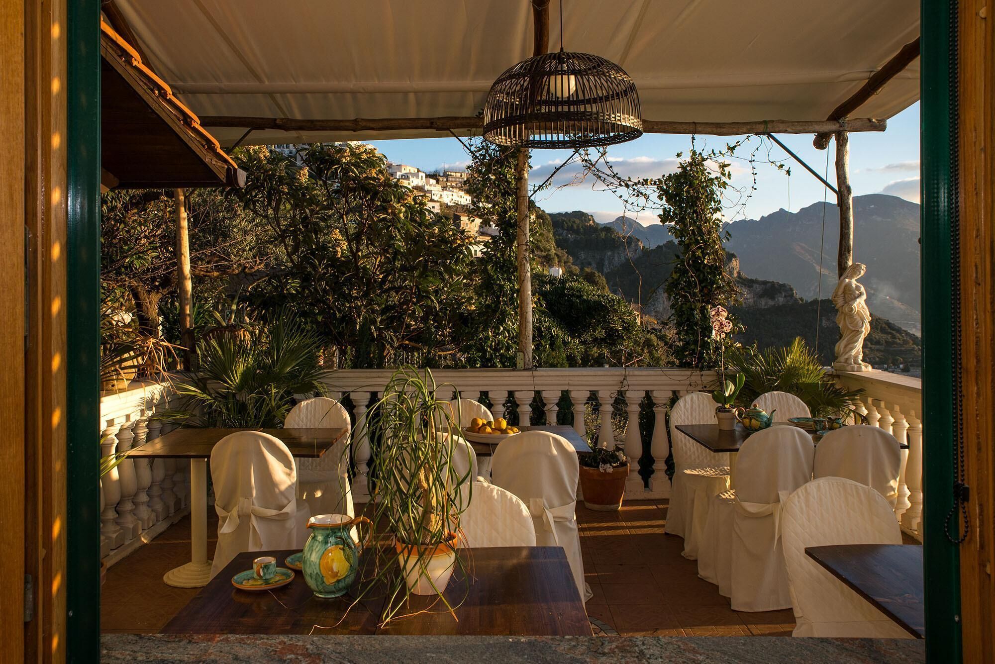 A terrace with white chairs and tables, a hanging light fixture, and a view of mountains.