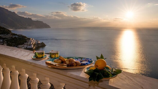 A balcony overlooking a coastal view with a table set with pastries, a plate of bread, and a bowl of fruit. - Villa Gioiello - Sea View Pool With Chromotherapy (Amalfi)
