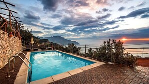 A swimming pool with a stone wall and a view of the sea and mountains during sunset. - Villa Gioiello - Sea View Pool With Chromotherapy (Amalfi)