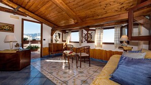 A cozy room with wooden ceiling beams, a bed with a blue and yellow blanket, a wooden dresser, a chair, and a small table with a lamp. - Villa Gioiello - Sea View Pool With Chromotherapy (Amalfi)