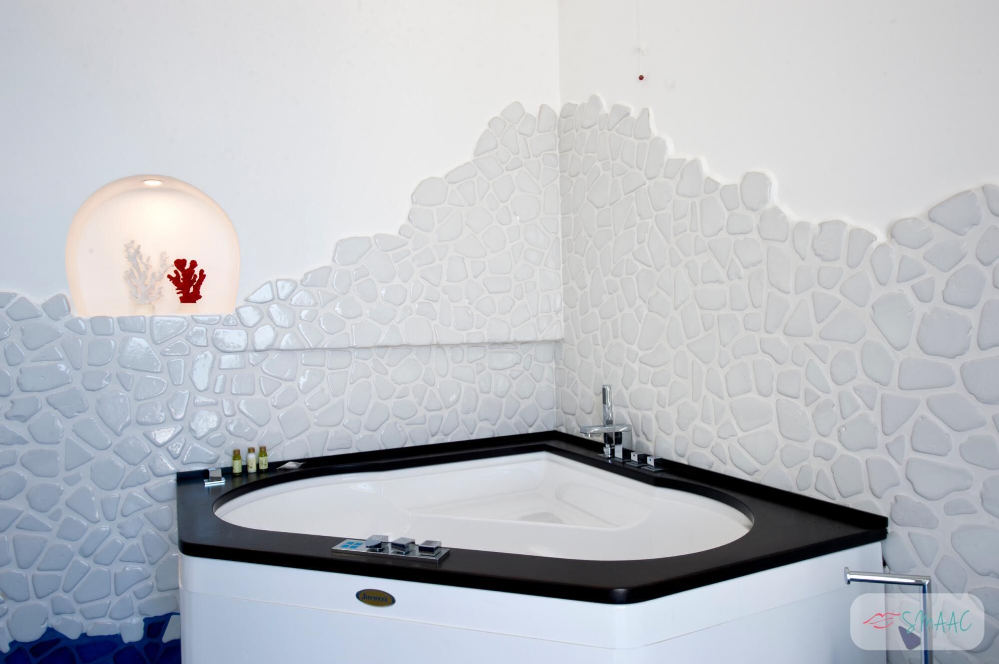 Un baño moderno con una bañera independiente, una lámpara de pared y un adorno de coral.
