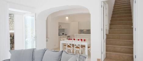 Um interior moderno com um sofá cinza, uma cozinha com armários brancos e uma escada de madeira.