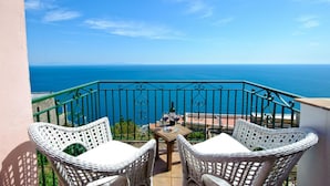 Ein Balkon mit Korbstühlen und einem Tisch, mit Blick auf das klare, blaue Meer.