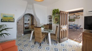 Een eetgedeelte met rieten stoelen, een glazen tafel en een hanglamp.
