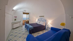 Een slaapkamer met een bed, een bank, een tafeltje en uitzicht op zee.