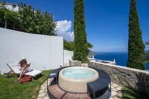Un espace extérieur privé comprenant un jacuzzi, des chaises longues et une vue sur la mer.