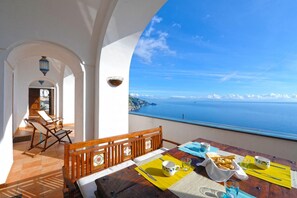 Uma área de refeições com uma mesa posta para dois, com vista para a paisagem costeira.