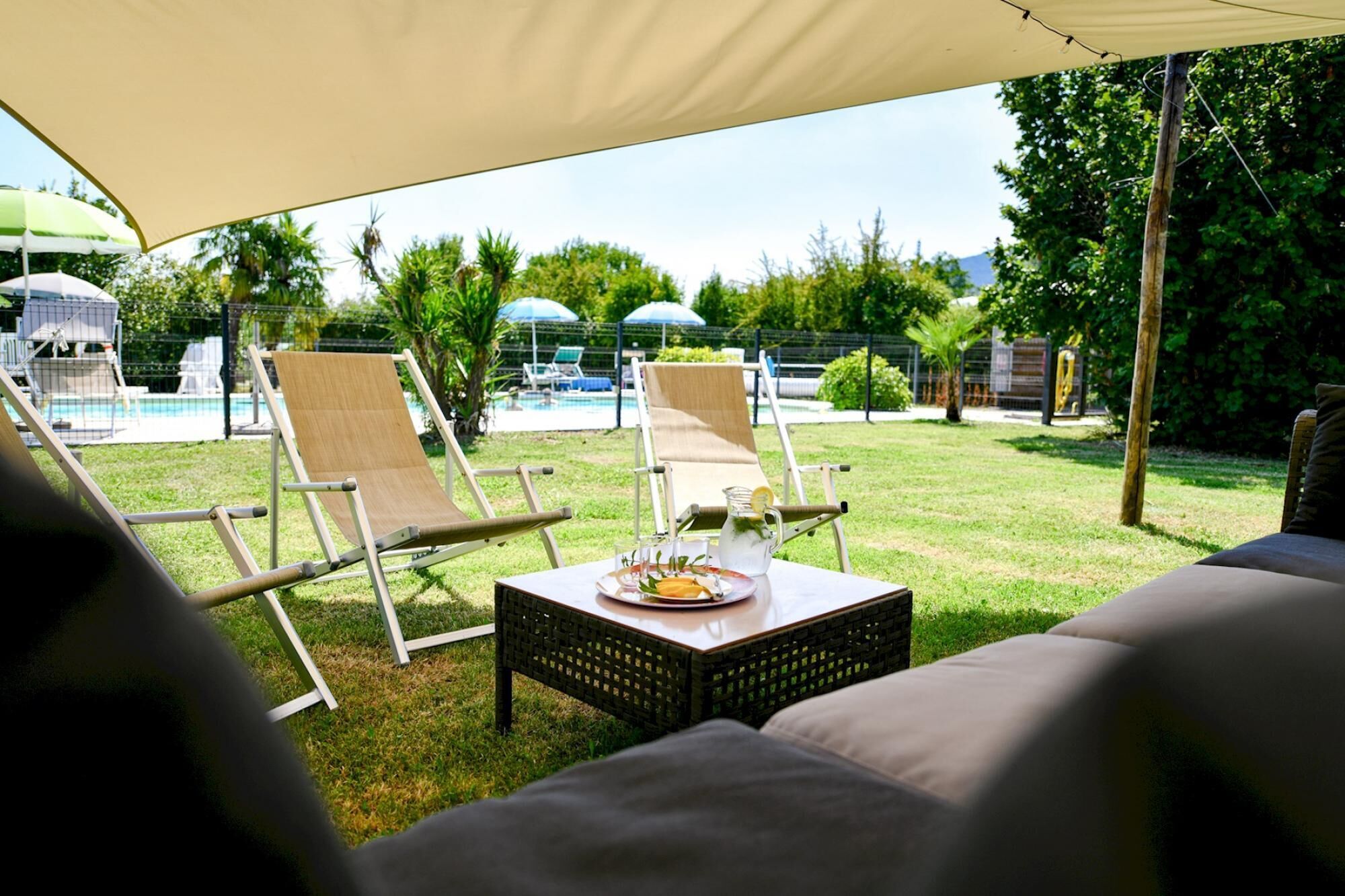A patio area with outdoor seating, a table with a pitcher of iced tea, and a pool in the background.