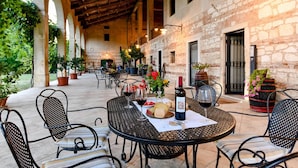 An outdoor patio area with round tables and chairs, stone walls, and potted plants. - Rosmarino Apartment With two Bedrooms and one Bathroom on the Ground Floor Apartment 1 (Longare)