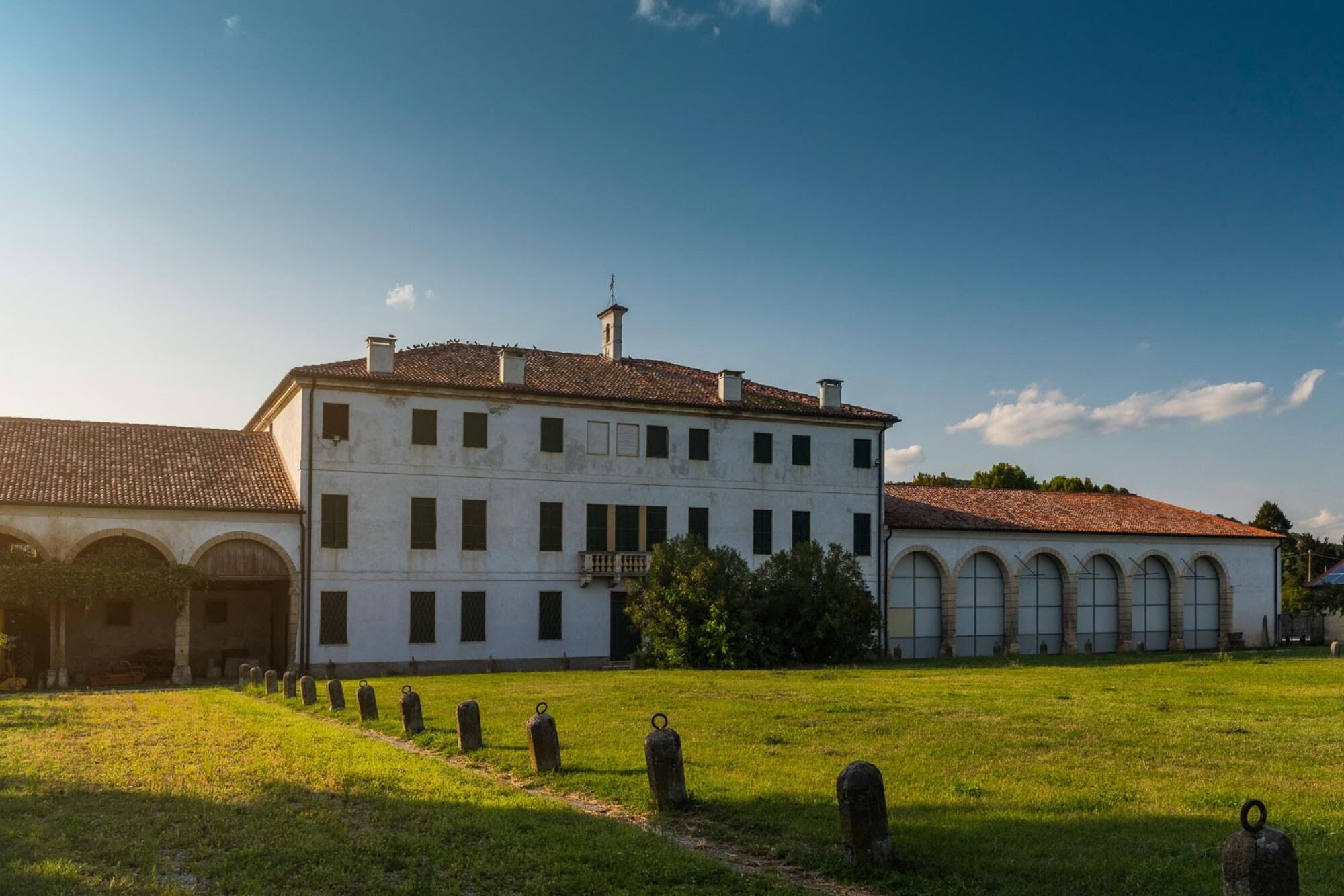 A large white building with a tiled roof, surrounded by a grassy area with gravestones.