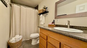 A bathroom with a toilet, sink, and shower curtain. There is a towel rack with a basket and toiletries. - Rustic, pet-friendly Olympia cottage on wooded acres with patio, fire pit, and modern comforts (Olympia)