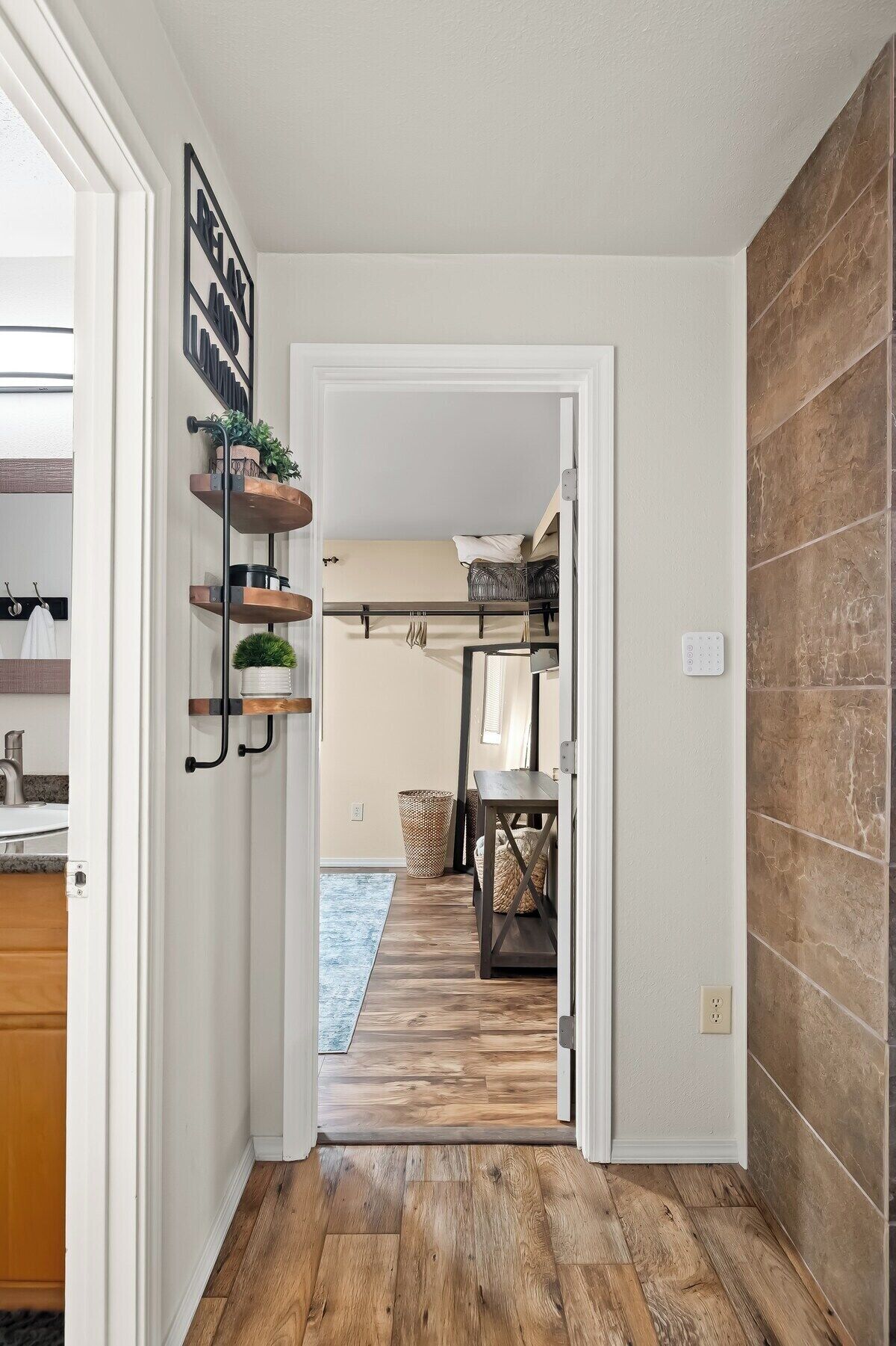 A hallway leading to a bedroom with a bed, a bedside table, and a wall-mounted shelf with plants.