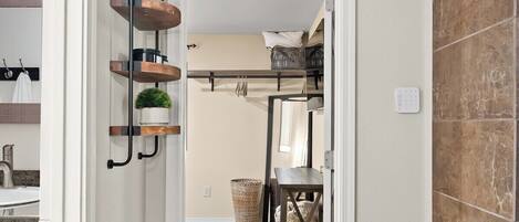 A hallway leading to a bedroom with a bed, a bedside table, and a wall-mounted shelf with plants.