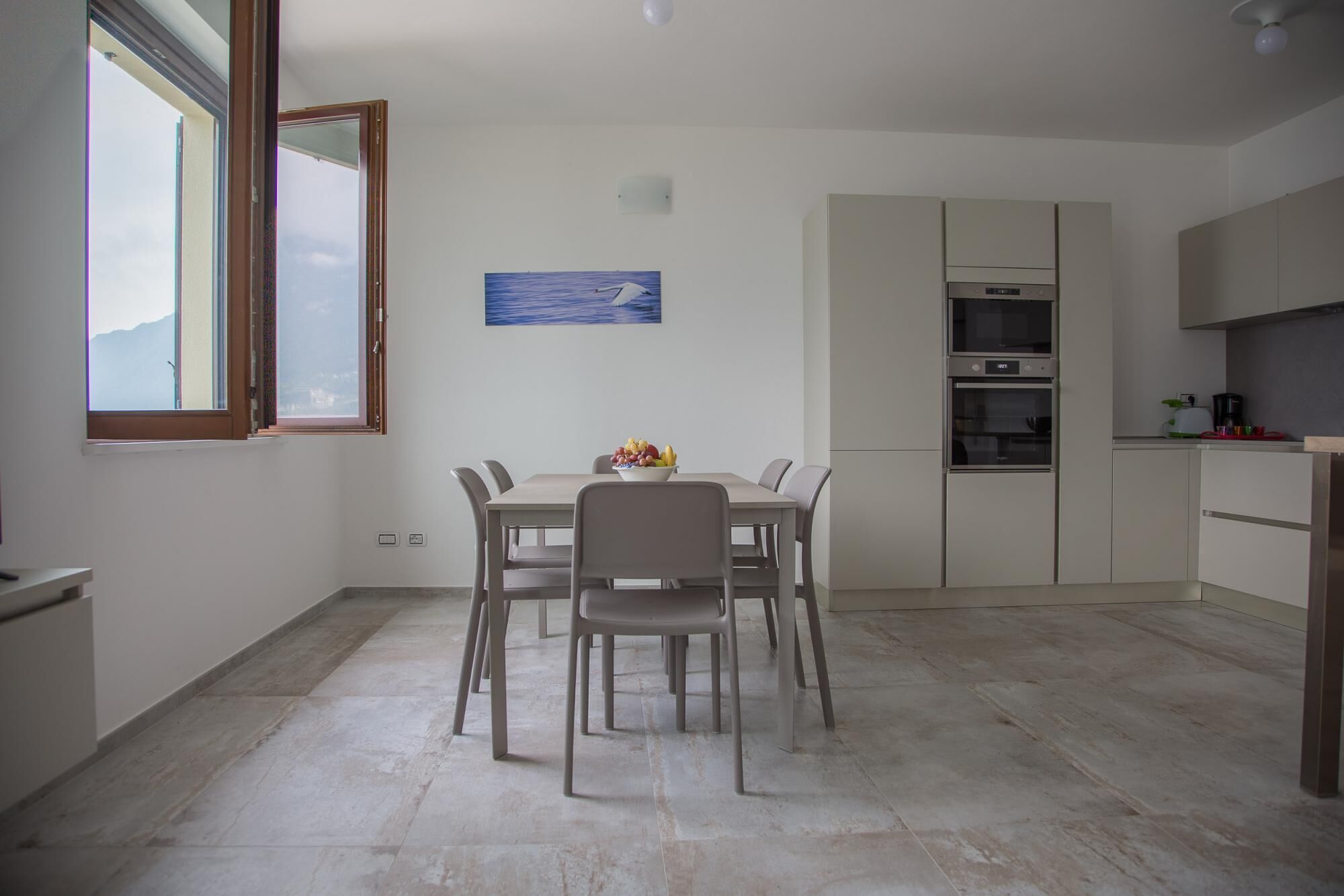 Una cocina moderna con una mesa y sillas, un cuadro en la pared y vistas por una ventana.