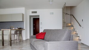 A modern living room with a grey sofa, a red pillow, a dining area with a table and chairs, and a staircase. - C0-e569-lbag97a2 - Dream Lake Apartment 1 (Lezzeno)