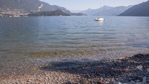 A lake with a boat, pebbly shore, and mountains in the background. - C0-e569-lbag97a2 - Dream Lake Apartment 1 (Lezzeno)