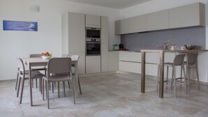 A modern kitchen with a dining area, featuring a table and chairs, a built-in oven, and a countertop with a kettle and cups. - C0-e569-lbag97a2 - Dream Lake Apartment 1 (Lezzeno)