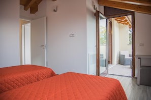 A bedroom with two beds, a sliding glass door leading to an outdoor area with furniture.