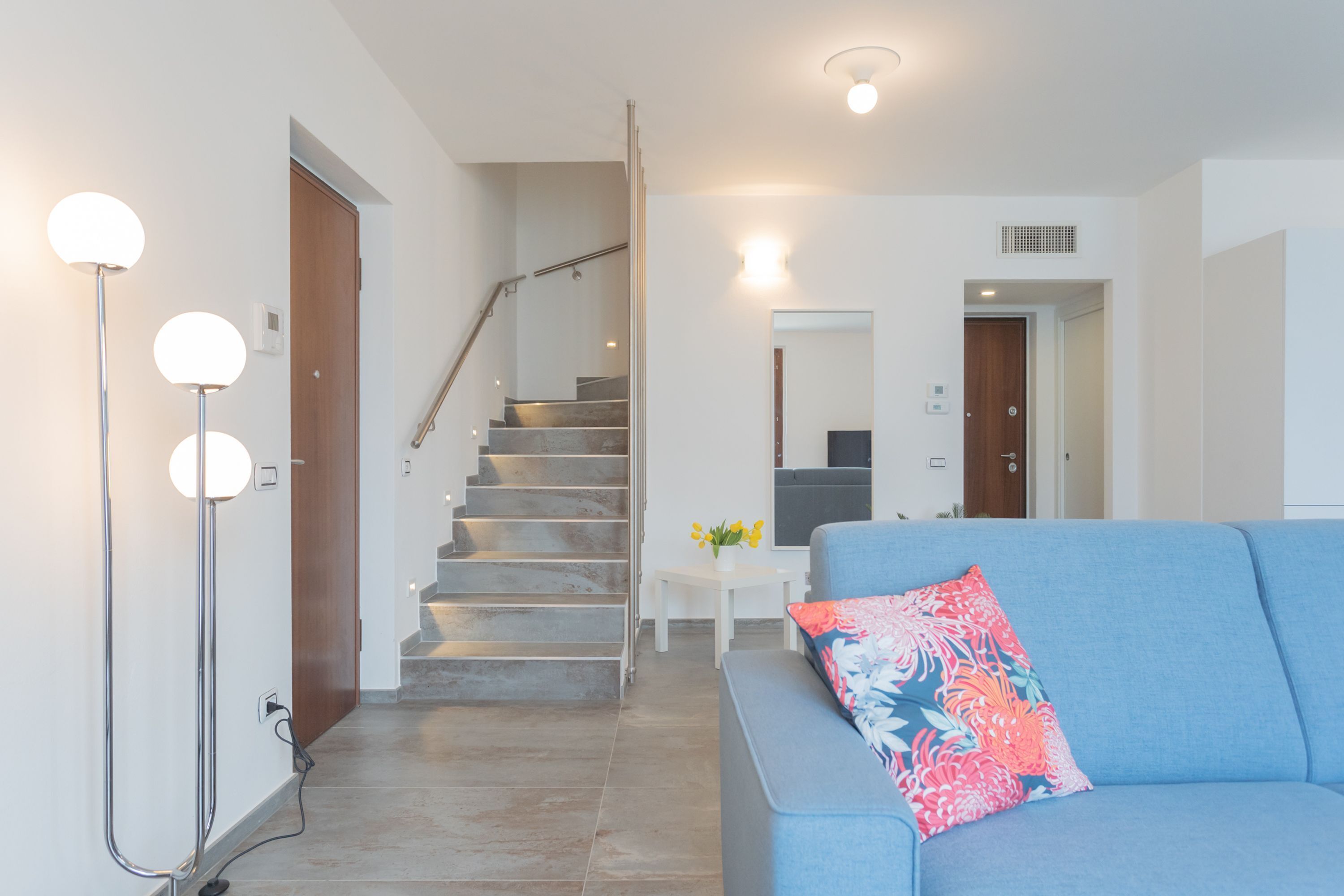 Una sala de estar moderna con un sofá azul, una escalera y una pared blanca.