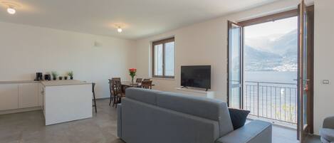 A modern living room with a grey sofa, a TV, and a balcony with a view of a city and mountains.