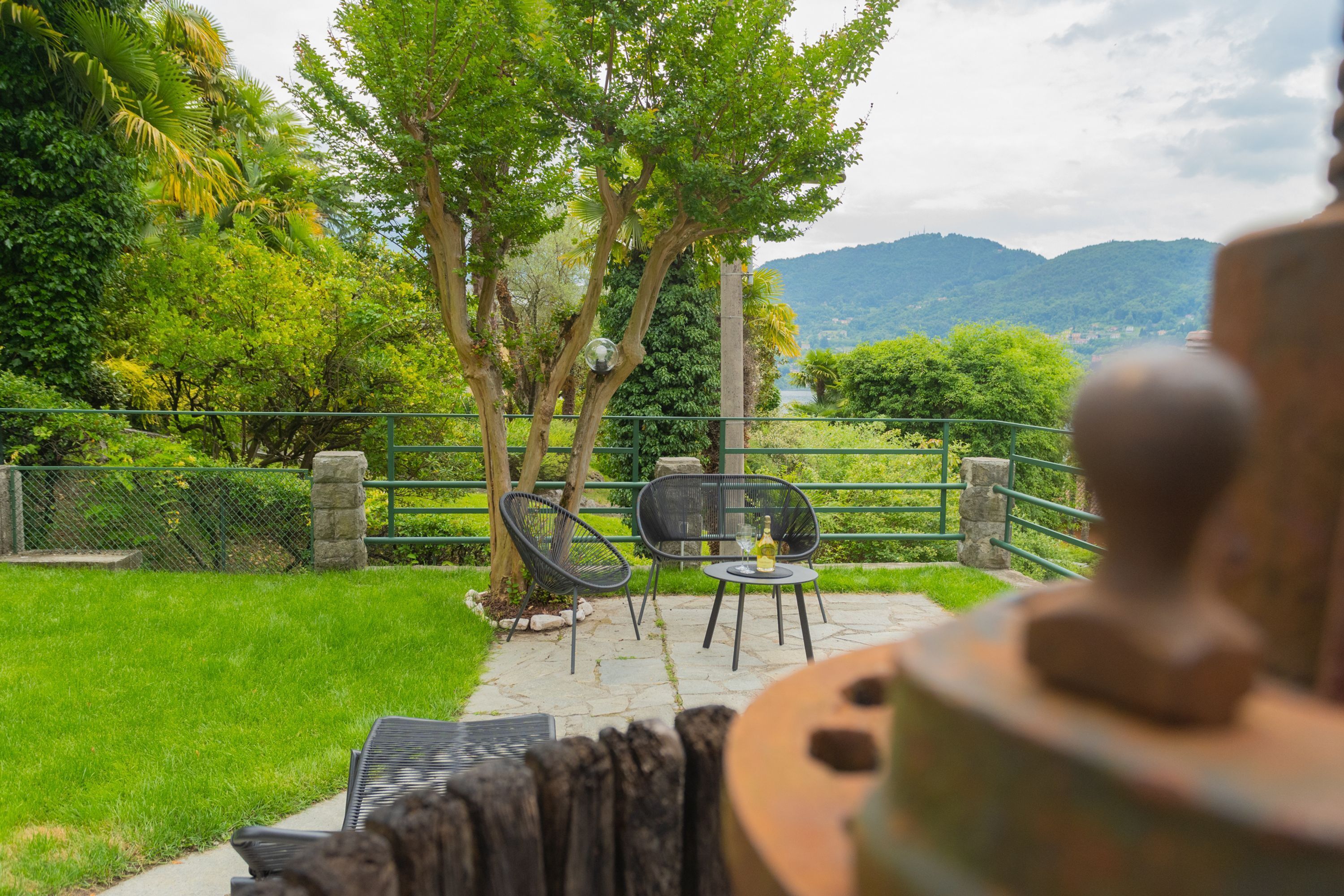 Un patio exterior con vistas a un paisaje montañoso, una mesa con sillas y una escultura decorativa.