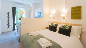 Ein Hotelzimmer mit einem großen Bett, einer grünen Tagesdecke, zwei Kissen, einem Nachttisch, einem Spiegel und Blick ins Freie.