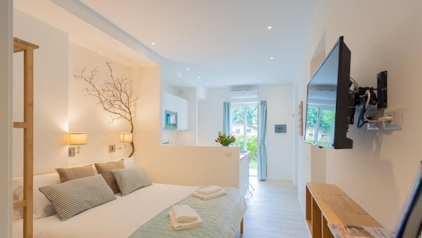 A modern hotel room with a large bed, bedside lamps, a TV mounted on the wall, and a wooden bench. - Co-f181-carb1bt - Tremezzo Apartment 2 (Tremezzina)