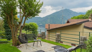 An outdoor patio with wicker furniture, a stone table, and a view of mountains and a lake. - Co-f181-carb1bt - Tremezzo Apartment 2 (Tremezzina)