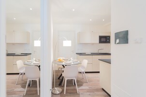 Cocina moderna con armarios blancos, microondas y comedor con mesa redonda y sillas blancas.