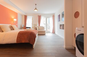 Habitación de hotel con cama, escritorio, silla, lavadora y vistas al exterior.