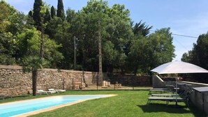 Un patio trasero con piscina, sillas de descanso y un muro de piedra.