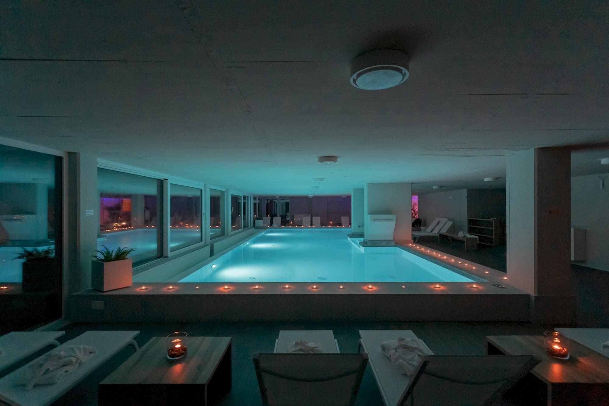 A swimming pool with a view of the city at night, surrounded by lounge chairs and tables with candles.