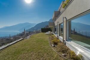 Un edificio moderno con grandes ventanales que dan a un paisaje montañoso y una masa de agua.