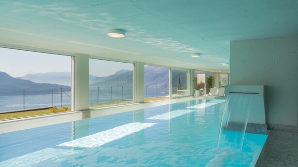 Une piscine intérieure dotée de grandes fenêtres offrant une vue sur les montagnes et un plan d’eau.