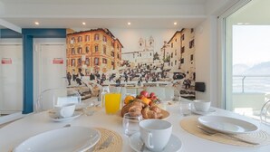 Une table de petit-déjeuner dressée avec des assiettes, des tasses et un arrangement de fruits, avec une fresque représentant un paysage urbain en arrière-plan.