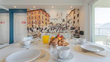 A breakfast table set with plates, cups, and a fruit arrangement, with a cityscape mural in the background.