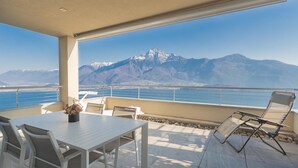 Une terrasse avec une table et des chaises, offrant une vue sur un paysage montagneux et une étendue d’eau.