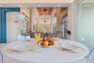Mesa de comedor lista para dos, con una fuente de frutas, vasos y una jarras de jugo de naranja.
